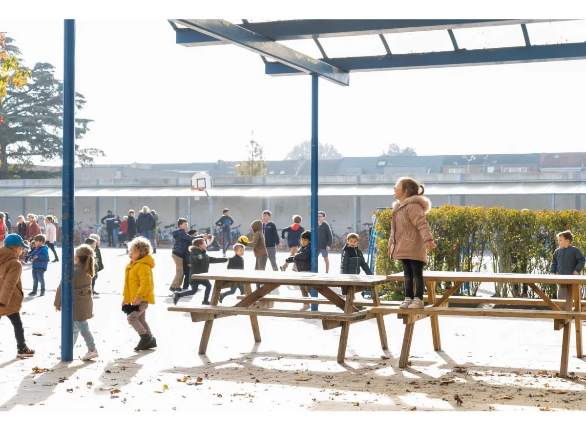 Speelplaats met spelende kinderen en één kind staat op een bank