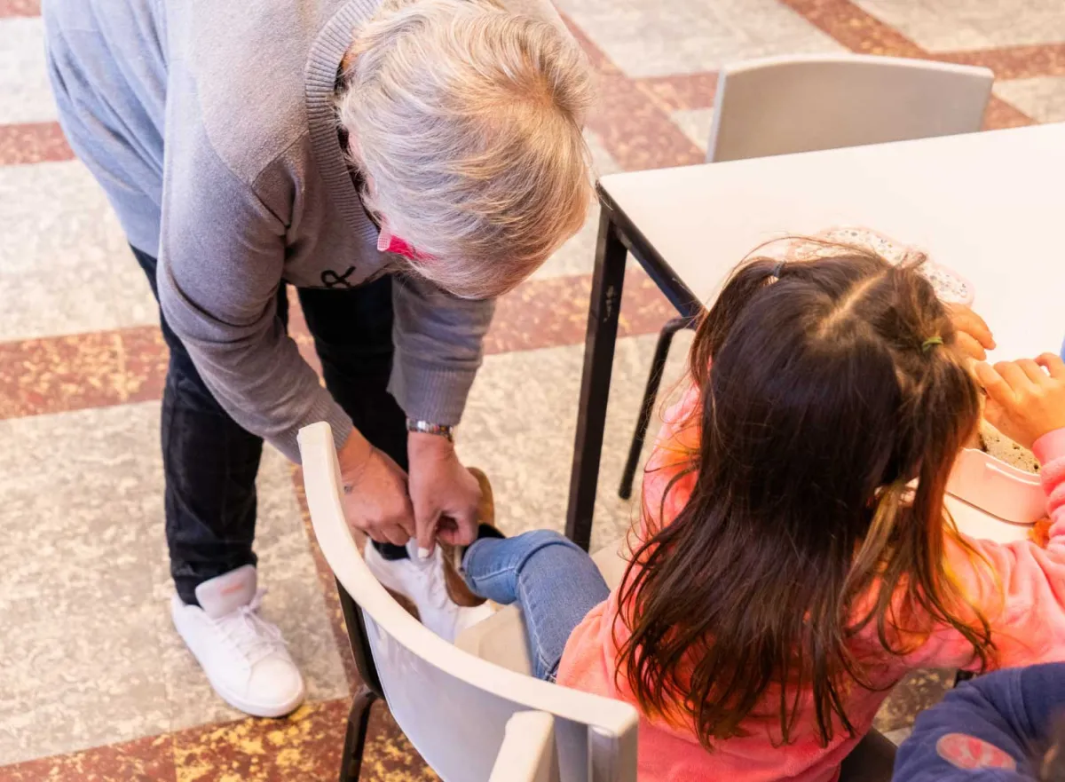 Middagbegeleider helpt kind met schoen