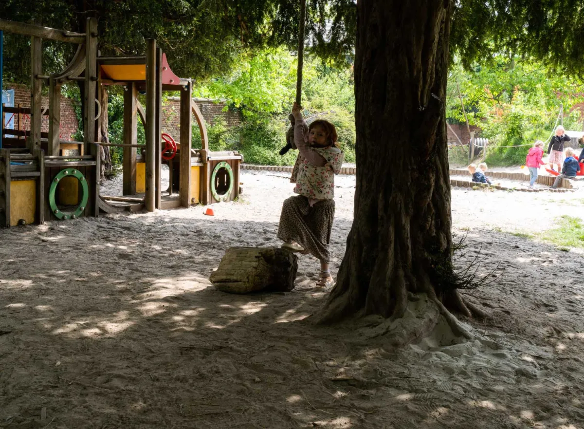Kind hangt aan touw aan boom op de speelplaats